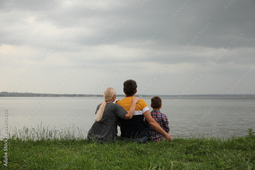 Cute little boy and grandparents spending time together near river, back view