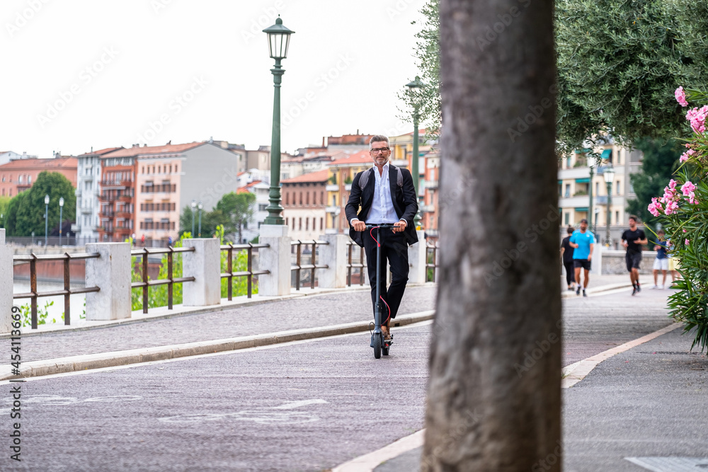 Young businessman in a suit riding an electric scooter while commuting to work in city. Ecological transportation concept