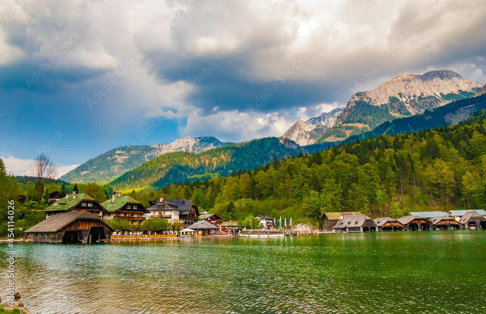 Fototapeta premium Lovely panoramic view of the village Schönau am Königssee with the alps in the background at the northern end of the Königssee lake in Bavaria, Germany. A boat is waiting at the pier.