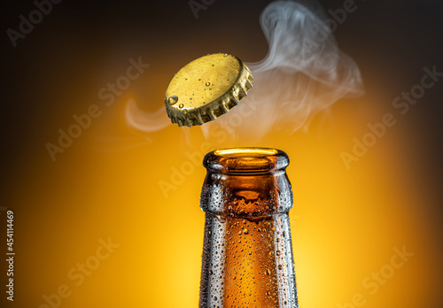 Opening of cold beer bottle - gas output and bottle cap in the air. Isolated on a yellow background. photo