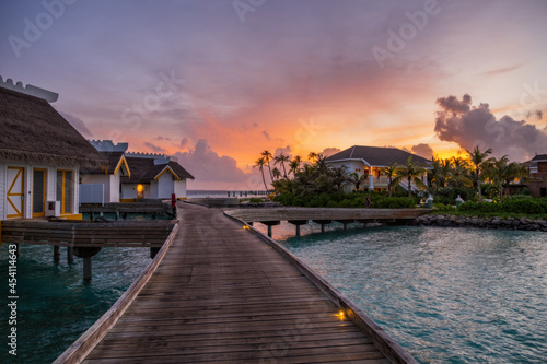 Fototapeta Naklejka Na Ścianę i Meble -  Over water bungalows with steps into amazing green lagoon at sunset time. Crossroads Maldives, july 2021