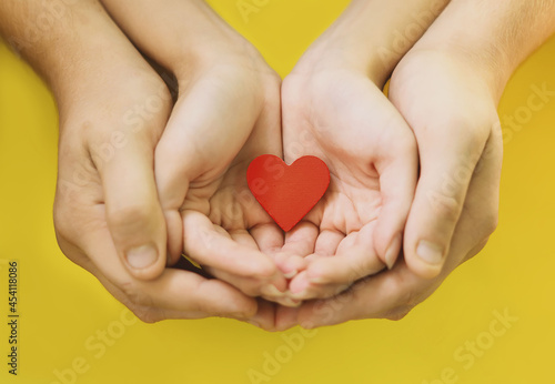 Young  loving people with a red heart in their palms. The hands of a man and a woman holding together a heart  a symbol of love  on a yellow background. The concept of Valentine s Day. Happy family