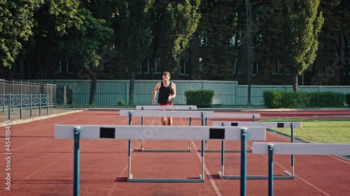 Professional athlete overcomes obstacles by jumping over them. Medium shot of a running track and field athlete at an outdoor urban stadium