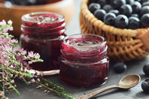 Fotografie Two jars of blueberry jam, basket with fresh blueberries on kitchen table