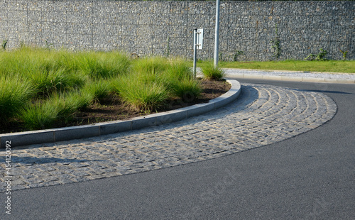 roundabout of gray granite cubes closer to the center. beveled concrete curbs with flowers and grass in the middle of the circle. half of the circle is passable through for firefighters