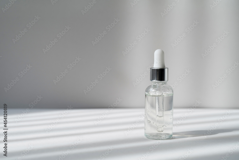 Serum in transparent bottle with white and silver cap on the grey background in with light and shadow stripes. Essence in glass dropper bottle. Skin care cosmetic product for branding. Copy space. Serum in transparent bottle with white and silver cap on the grey background in with light and shadow stripes. Essence in glass dropper bottle. Skin care cosmetic product for branding. Copy space.