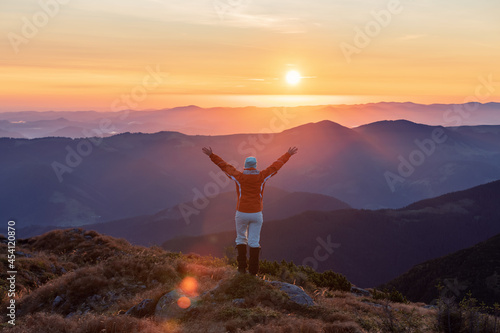 Landscape with high mountains. Successful tourist in sport clothes is standing at the edge of the precipice. Beautiful sunrise on the autumn morning. The lawn with orange grass. Wallpaper background.
