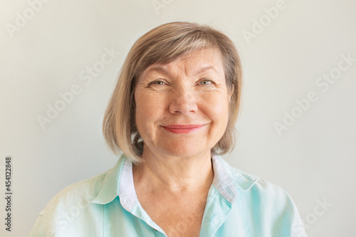 Happy senior woman with gray hair relaxing smiling is looking at the camera on a gray background