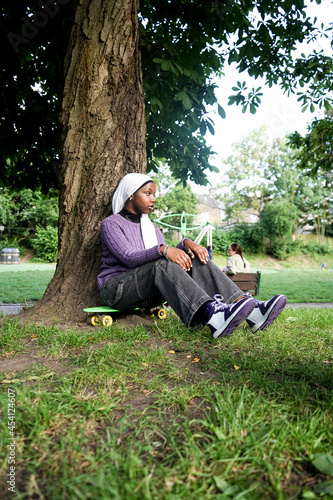Young woman wearing hijab sitting on skateboard in park