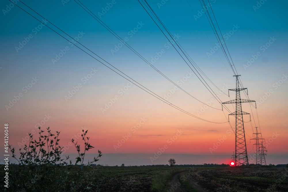Fototapeta premium Electricity pole with silhouette sunset sky, Electricity pylon with shadow of tree in dawn time, Electricity power transmission line on sunset with copy space