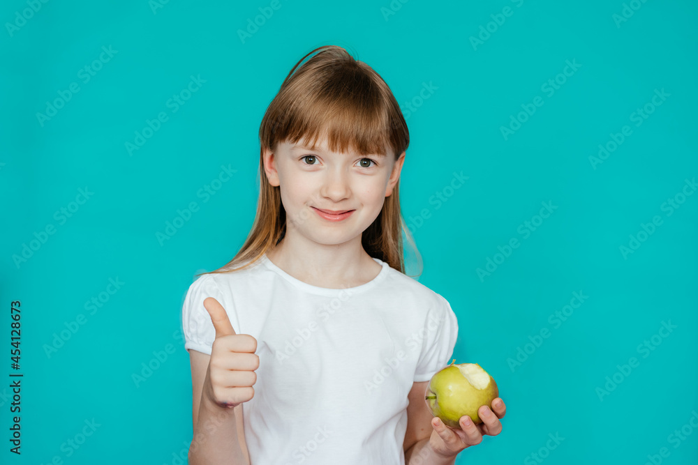 cute girl in a white t-shirt on a turquoise background bites an apple cute girl in a white t-shirt on a turquoise background bites an apple