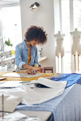 Obraz na plátne African-American dressmaker draws pattern using chalk and cardboard part in sewi