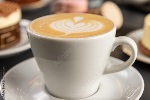 Primer plano de una taza blanca con cafe con dise  o de arte latte con macarones de fondo con foco diferenciado 