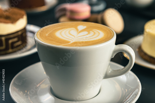 Caf    con arte latte en un primer plano acompa  ado de distintos tipos de tortas con foco diferenciado.