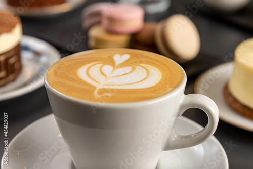 Caf    con arte latte en un primer plano acompa  ado de distintos tipos de tortas con foco diferenciado.