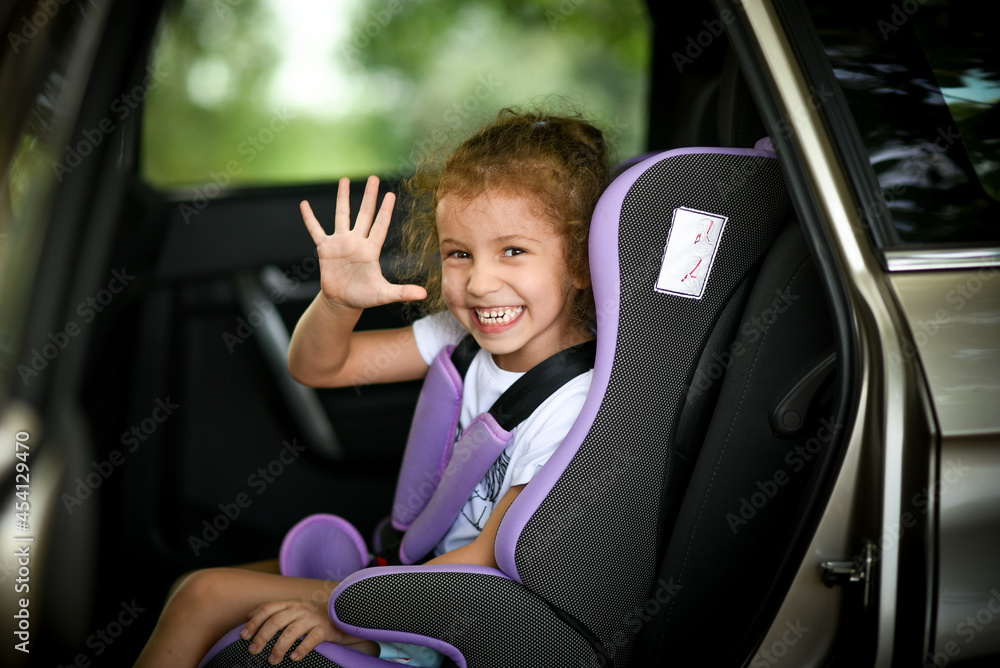 A liitle happy girl goes on a trip by car on a child safety seat summer vacation A liitle happy girl goes on a trip by car on a child safety seat summer vacation