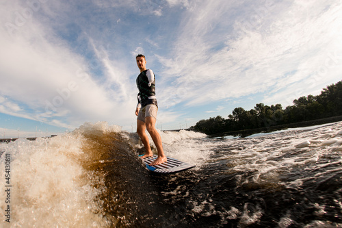 one-armed man is surfing on surfboard trails behind boat. Wakesurfing on the river