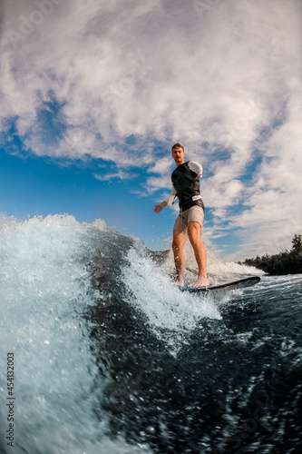 one-armed man ride the wave on wakeboard against the background of cloudy sky.
