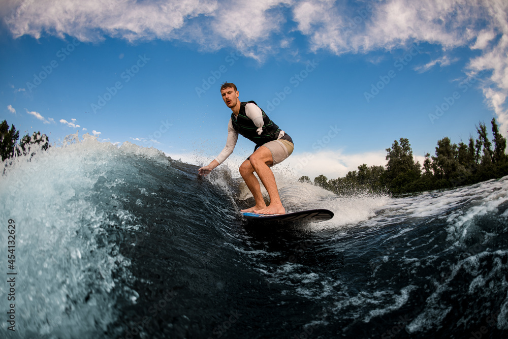 one-armed man wakesurfing on the board down the wave against the background of sky