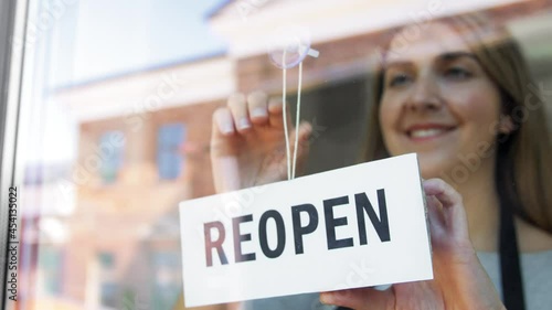 small business, reopening and service concept - happy smiling woman hanging reopen banner to window or door glass