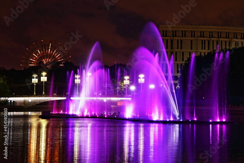 Colorful purple fountains on Svisloch River on the Ferris wheel background in the Yanka Kupala Park at summer night, a beautiful view of Minsk , a famous national landmark of the capital of Belarus
