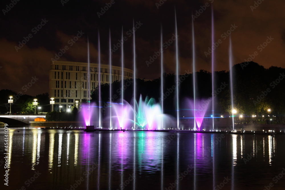 Colorful illuminated fountains on the Svisloch River at summer night on sky background , a beautiful view of Minsk , a famous national landmark of the capital of Belarus