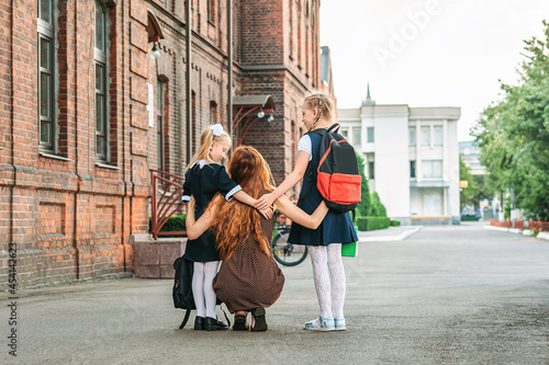 Mom leads the kids back to school. Two schoolgirl sisters. First day of study.