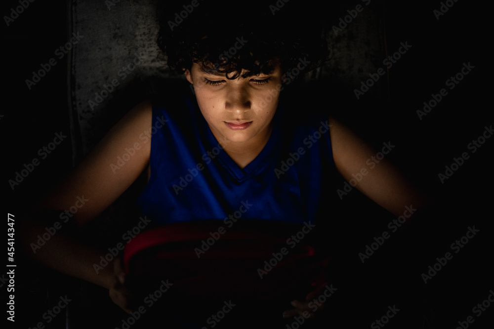 Joven en la oscuridad jugando con un tablet que ilumina su rostros Joven en la oscuridad jugando con un tablet que ilumina su rostros