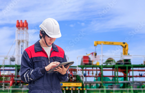 Young Asian engineer using digital tablet to working his job with blurred background of oil tanker in shipyard area