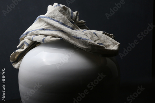 Un vaso in ceramica bianca e uno strofinaccio da cucina; composizione su fondo scuro  