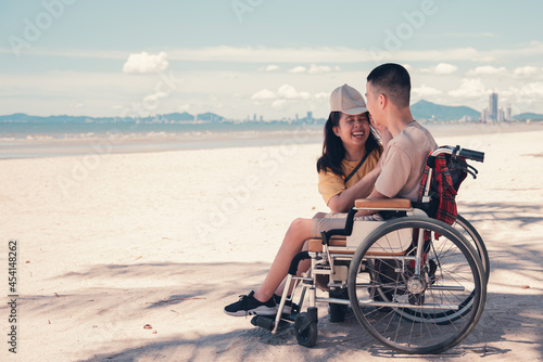 Happy mother take care to her son disabled teenage boy on wheelchair by love, Sea beach background, Lifestyle activities in travel of handicapped teen family.