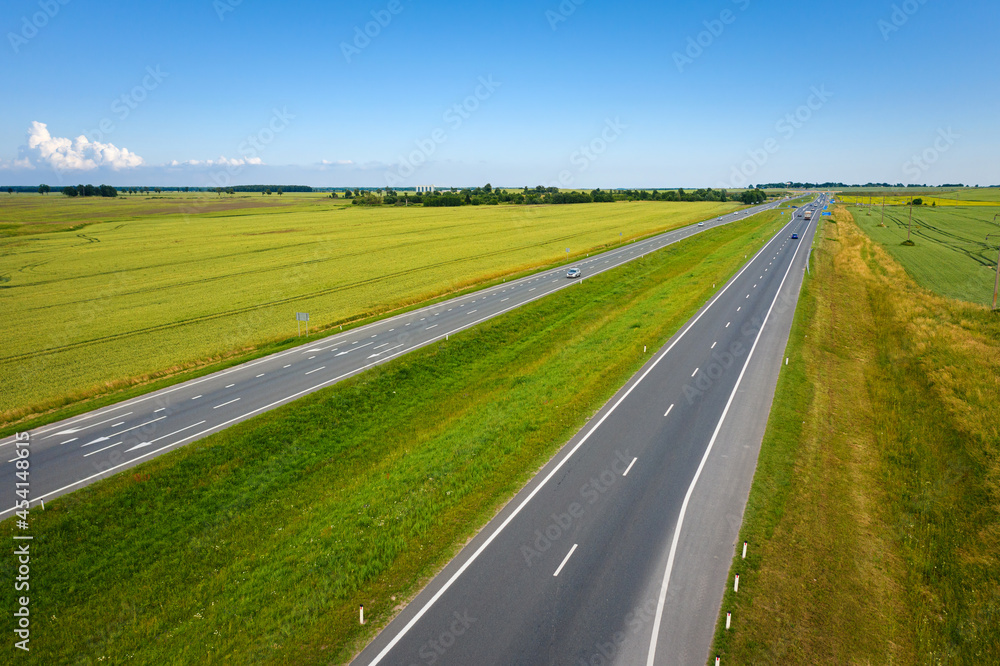 Fototapeta premium Asphalt highway through green summer field. Aerial view