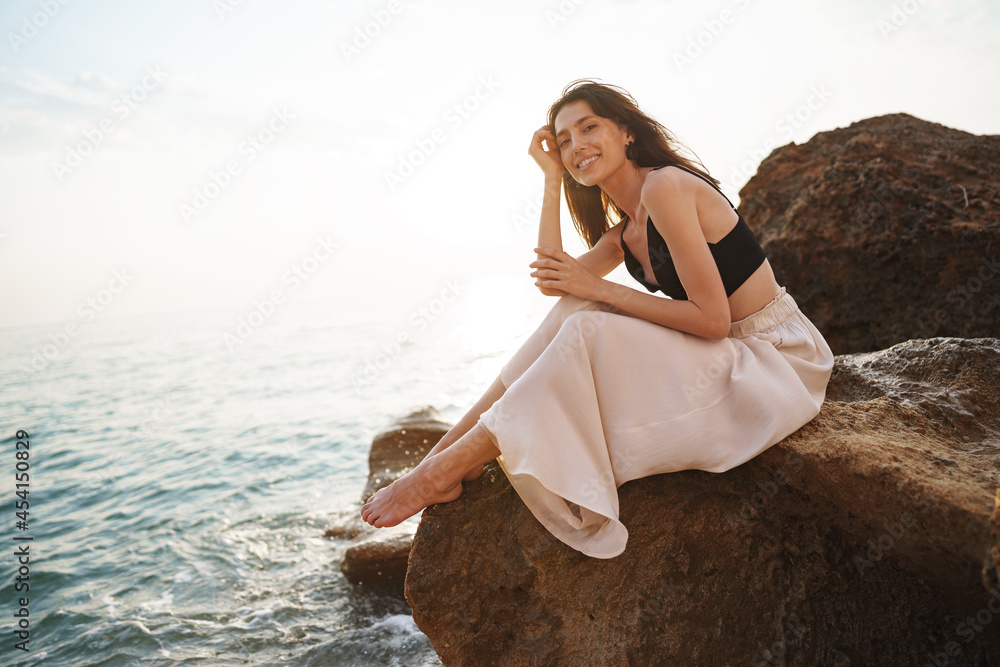 Woman traveler sitting near sea on cliff injoying view of sea and nature