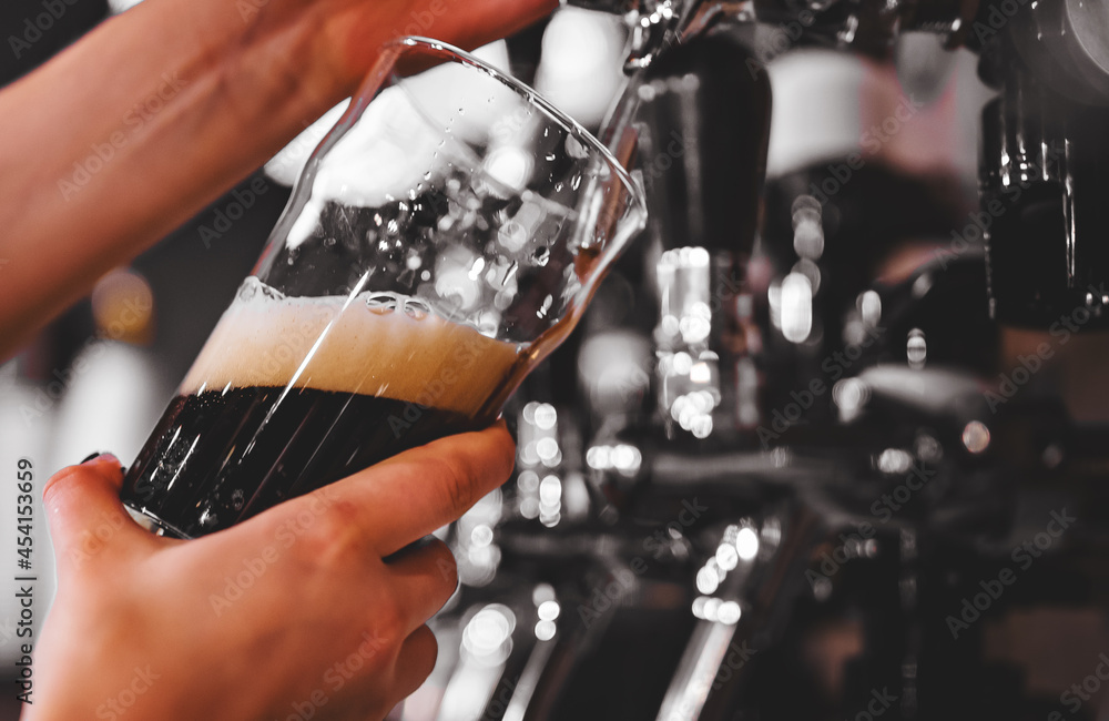 woman's hand holds a glass and pours dark foamy beer from the tap woman's hand holds a glass and pours dark foamy beer from the tap