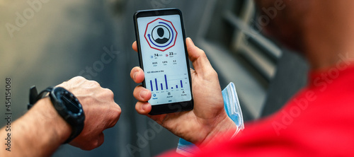 Close up of male hands using fitness app on smartphone. Man resting after jogging reading run results. Running man with Mobile phone connected to a smart watch recording data about sport activity.