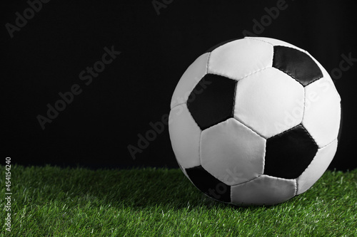 Football ball on green grass against black background. Space for text