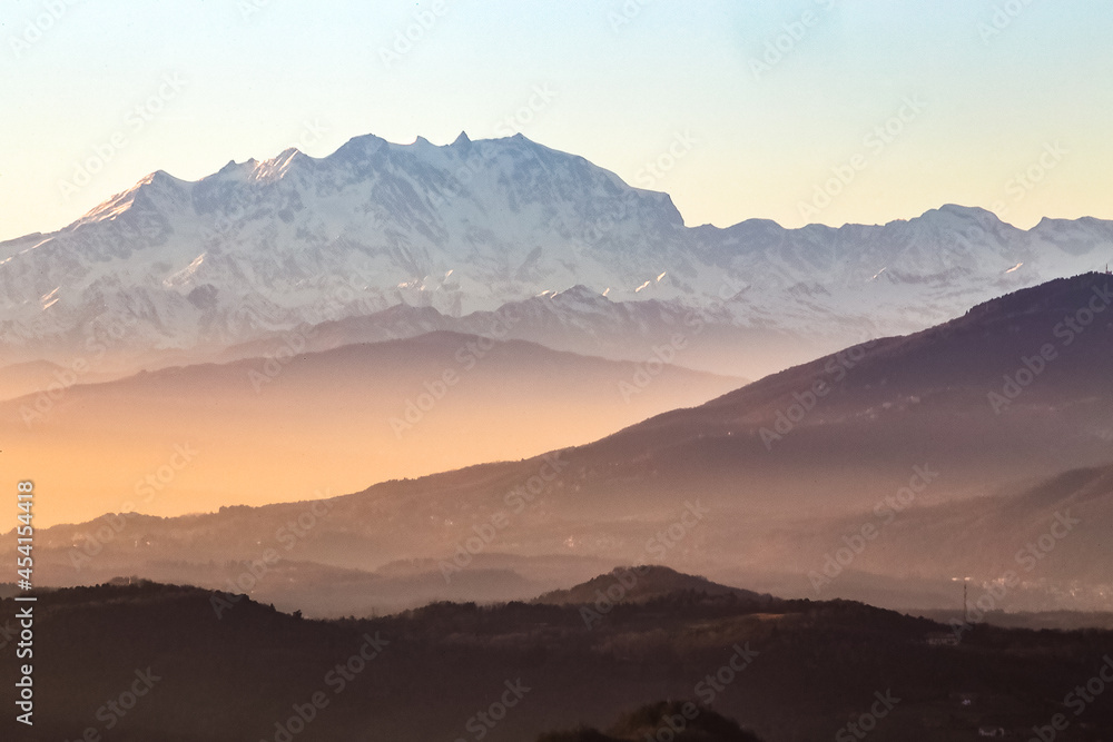 View of the misty and fog surrounding the mountains of the Italian Alps at winter sunset.  Layers of mountains. Nature tourism.