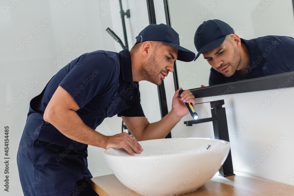 plumber checking sink with flashlight in modern bathroom plumber checking sink with flashlight in modern bathroom