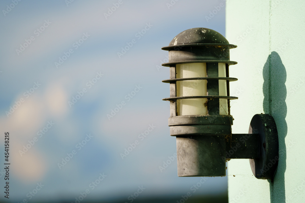 Old and dirty outdoor lamp on light green wall with copy space. Closeup of outdoor lamp in daytime.   
