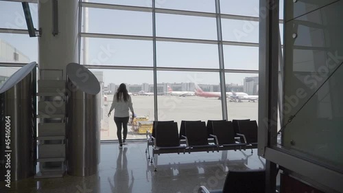 Woman walks airport near window, view airplane. Passenger going gate in terminal photo