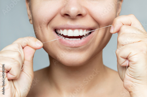 A cropped shot of a young beautiful caucasian woman flossing her teeth isolated on a gray background. Oral hygiene, dental health care, morning and evening routine. Close-up. Dentistry concept