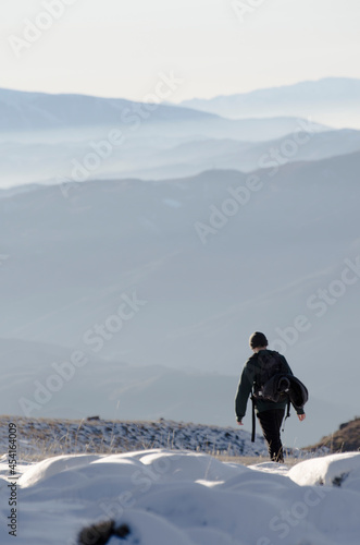 lonely man with backpack walking through a snowy high mountain landscape, he is above the clouds