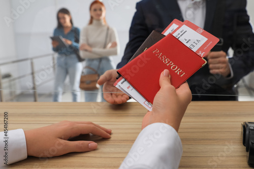 Agent giving passports with tickets to client at check-in desk in airport, closeup photo