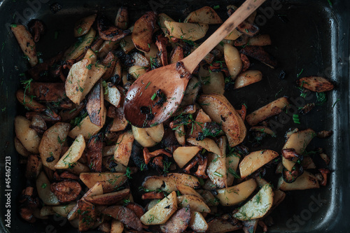 Fried potatoes with mushrooms and herbs in a pan with a wooden spoon