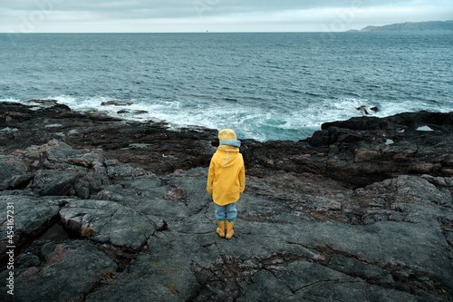 A child in a yellow raincoat looks at the ocean on a cold cloudy day