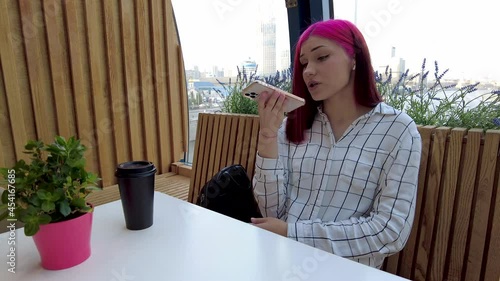 Beautiful red-haired student girl records voice message on smartphone for social networks sitting in caffe. High quality 4k footage photo