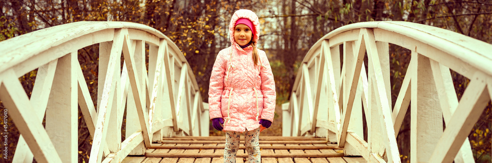 Φωτογραφία little happy six year old kid girl in autumn clothes stands on the humpback wooden bridge in the fall park