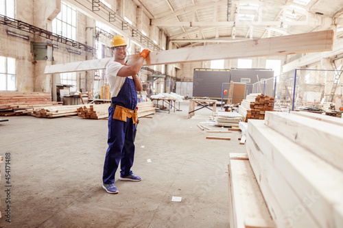 Cheerful male builder carrying wooden plank at construction site