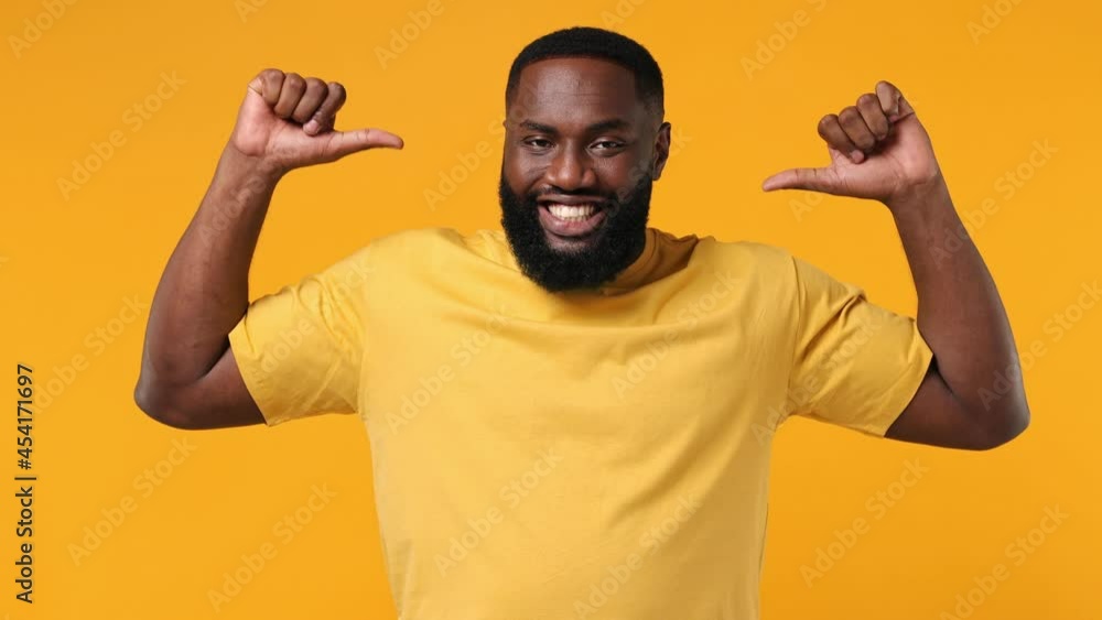 Confident smiling fun young bearded african american man 20s wears orange t-shirtpointing fingers on himself blinking showing thumb up like gesture isolated on plain yellow background studio portrait Confident smiling fun young bearded african american man 20s wears orange t-shirtpointing fingers on himself blinking showing thumb up like gesture isolated on plain yellow background studio portrait