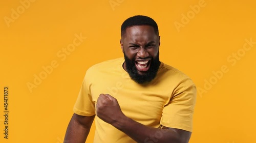 Excited jubilant overjoyed happy young bearded african american man 20s wears orange t-shirt doing winner gesture celebrate clenching fists say yes isolated on plain yellow background studio portrait photo